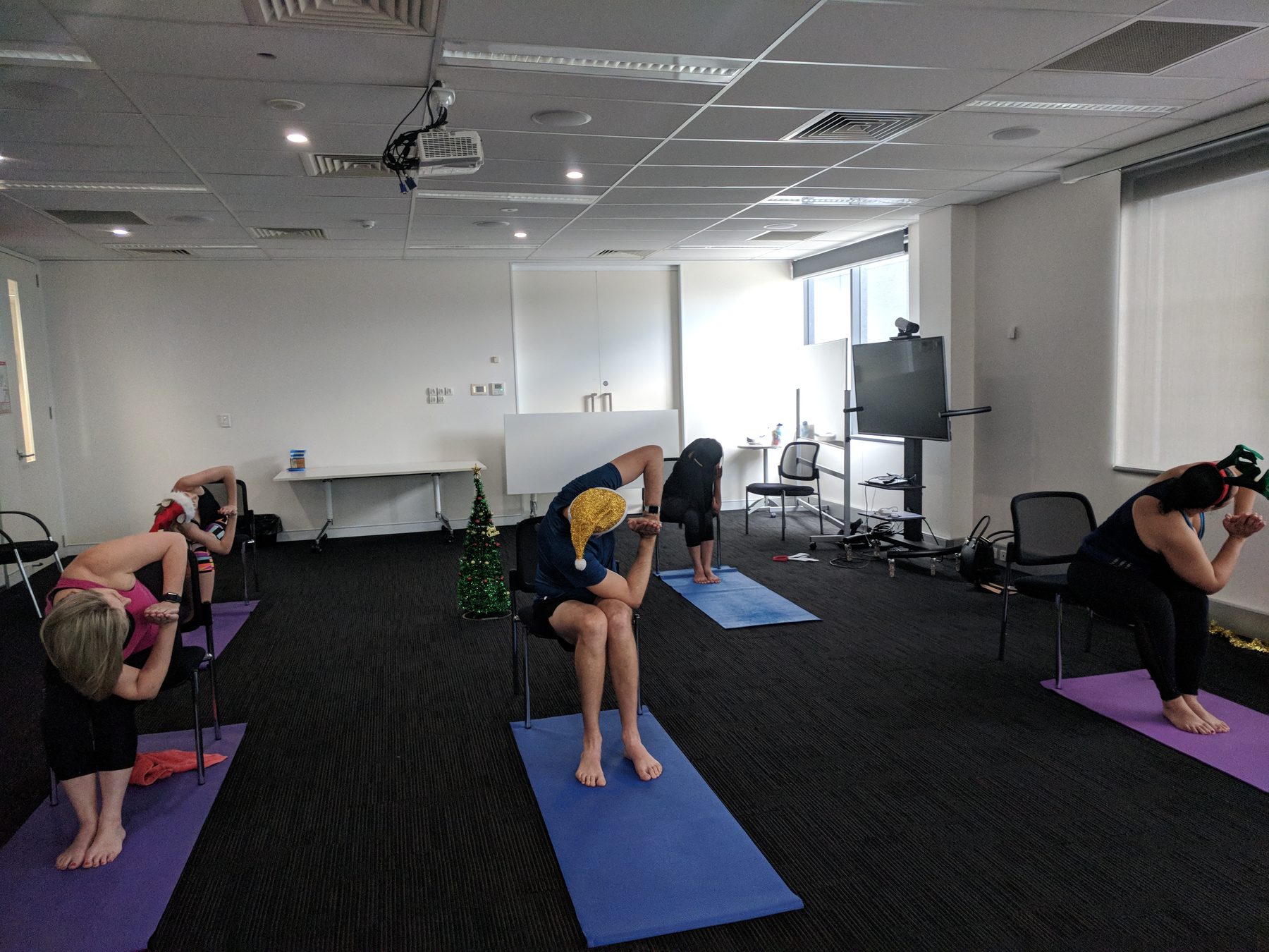 A small office yoga class of four stretching together in Christmas hats