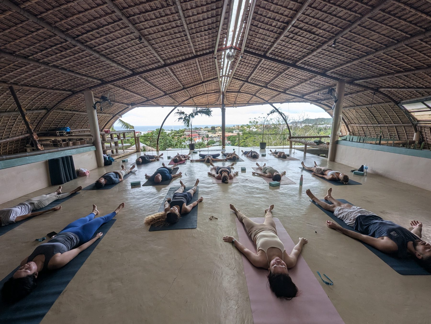 A group resting in savasana under an open-air bamboo studio overlooking the ocean