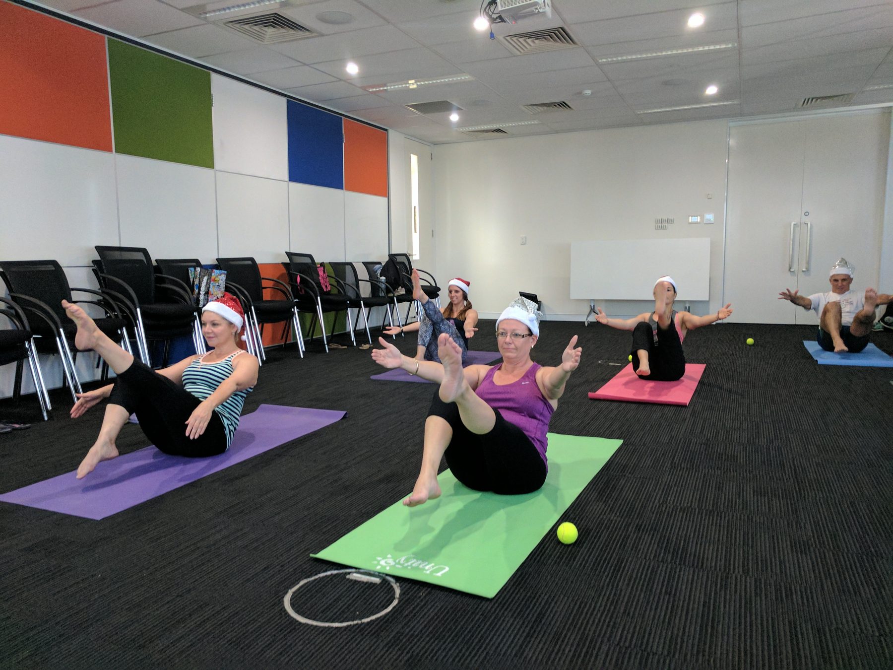 A team in Santa hats doing a seated core exercise together for an end-of-year celebration