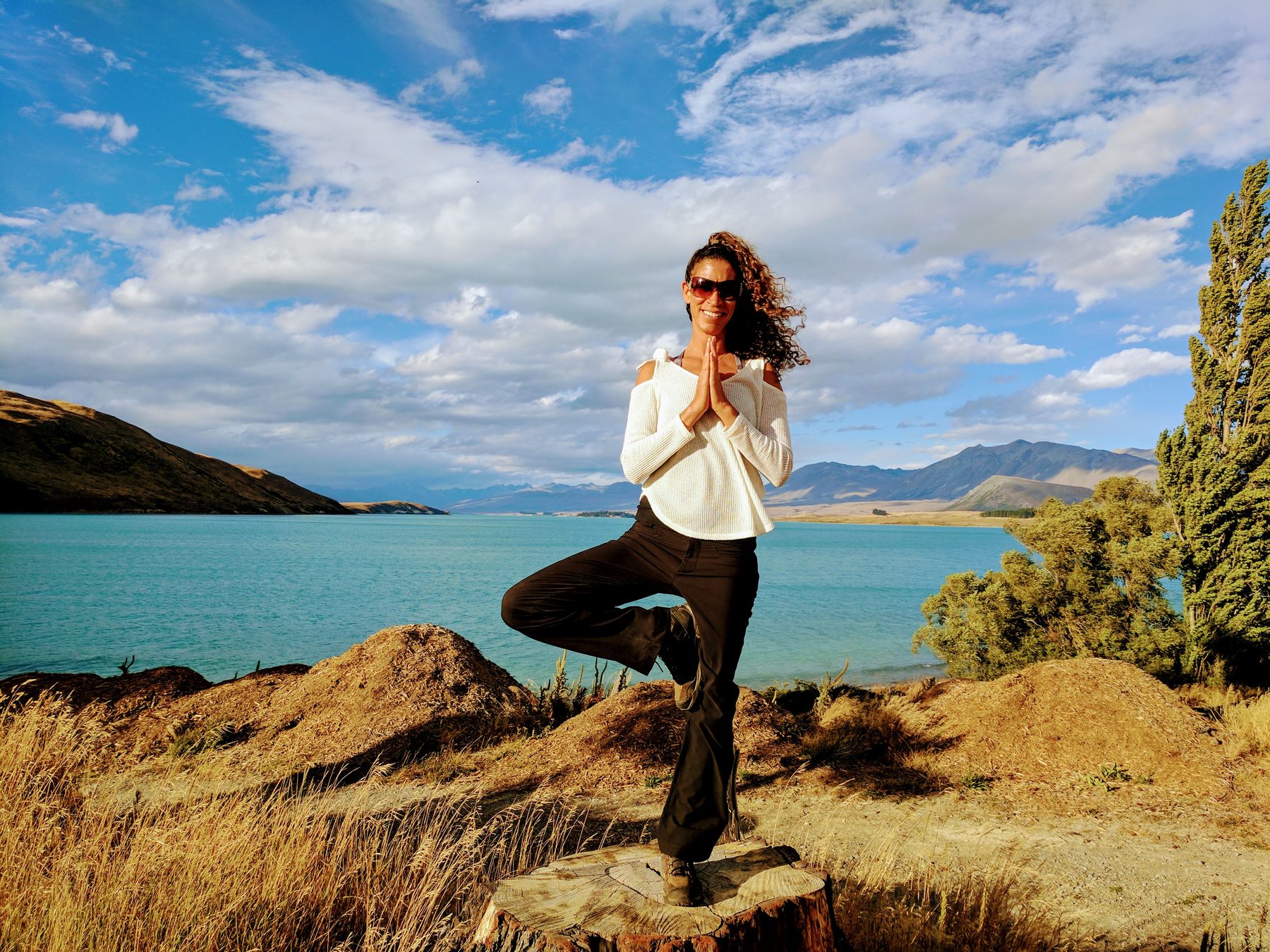 Shani in tree pose on a tree stump beside a lake