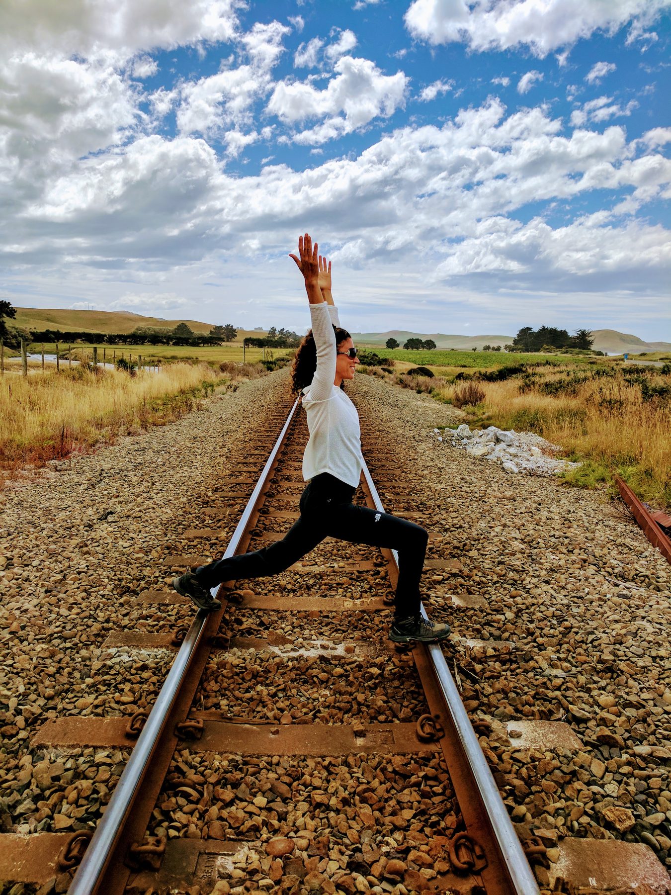 Shani in a warrior pose on a railway track surrounded by countryside